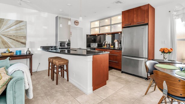 A modern kitchen with a central island, stainless steel appliances, and a dining area with wooden chairs. - 1 BR - Guesthouse - A beachside gem! Walk 1 min to Beach! (Boca Raton)
