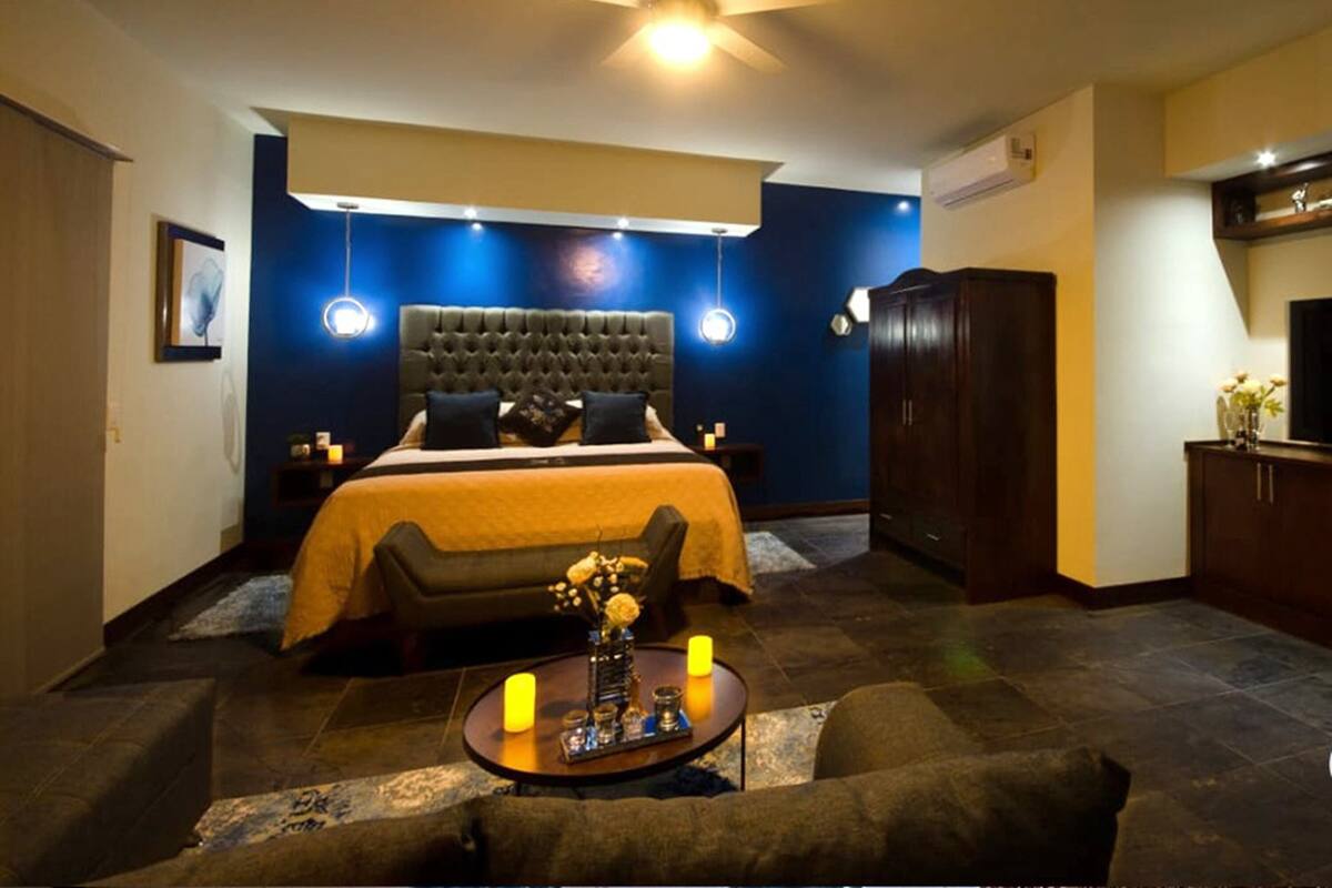 A bedroom with a large bed, bedside tables, a nightstand, a round coffee table with candles, and a ceiling fan.