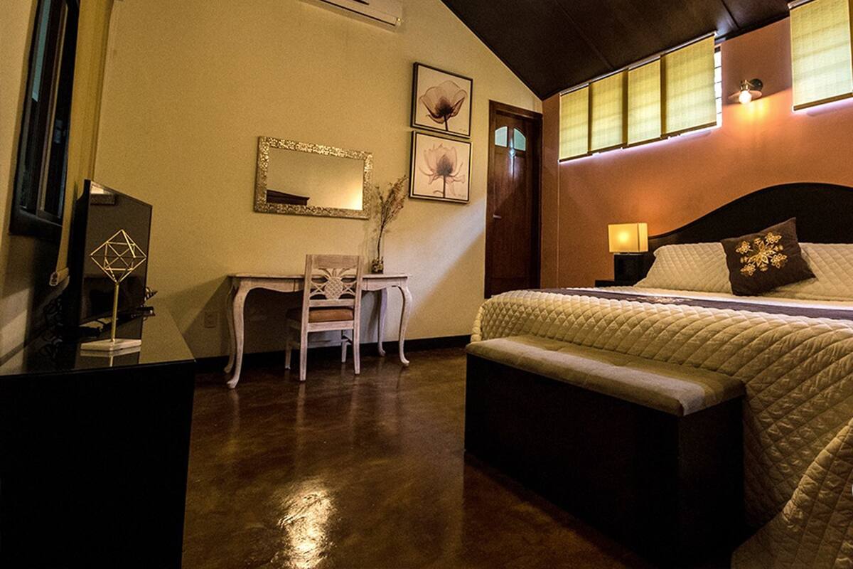 A bedroom with a bed, bedside table, lamp, and a desk with a chair.