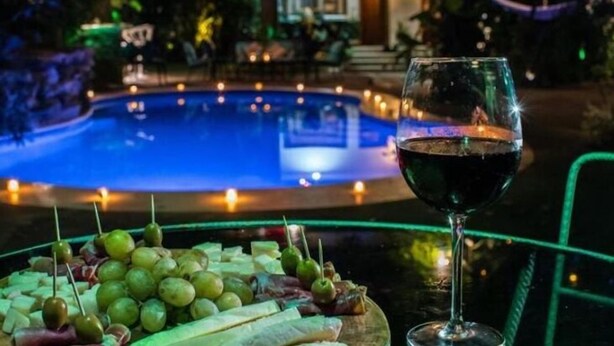 A poolside view with a glass of red wine and a fruit platter.