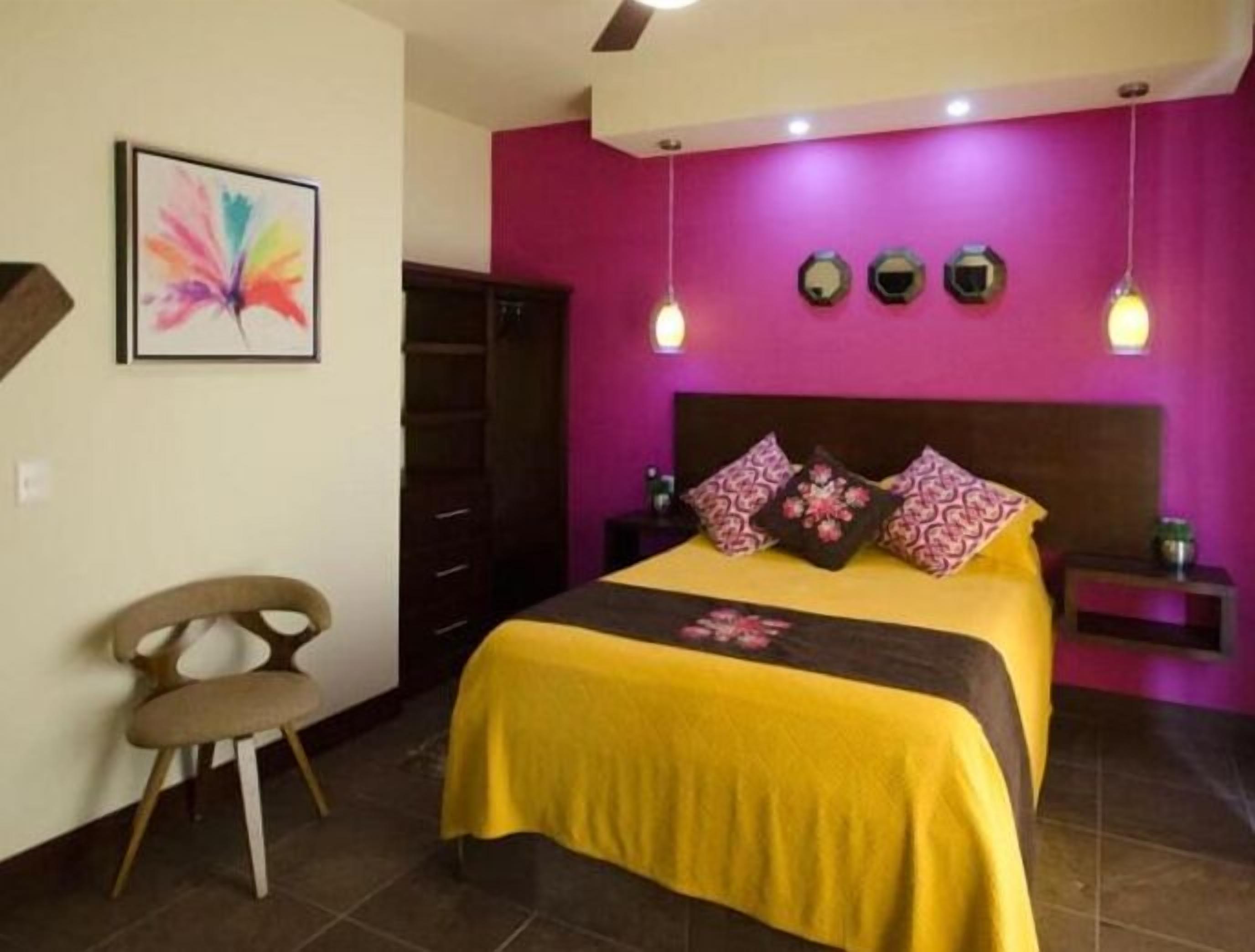 A bedroom with a bed, a chair, a dresser, and a wall with a colorful painting.