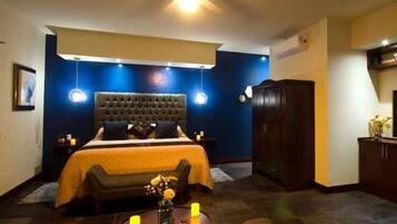 Ein Schlafzimmer mit einer gesteppten Kopfteil, einem Bett mit gelber Bettdecke, Nachttischen mit Lampen, einem dunklen Holzschrank und einem Fernseher auf einem Schrank.