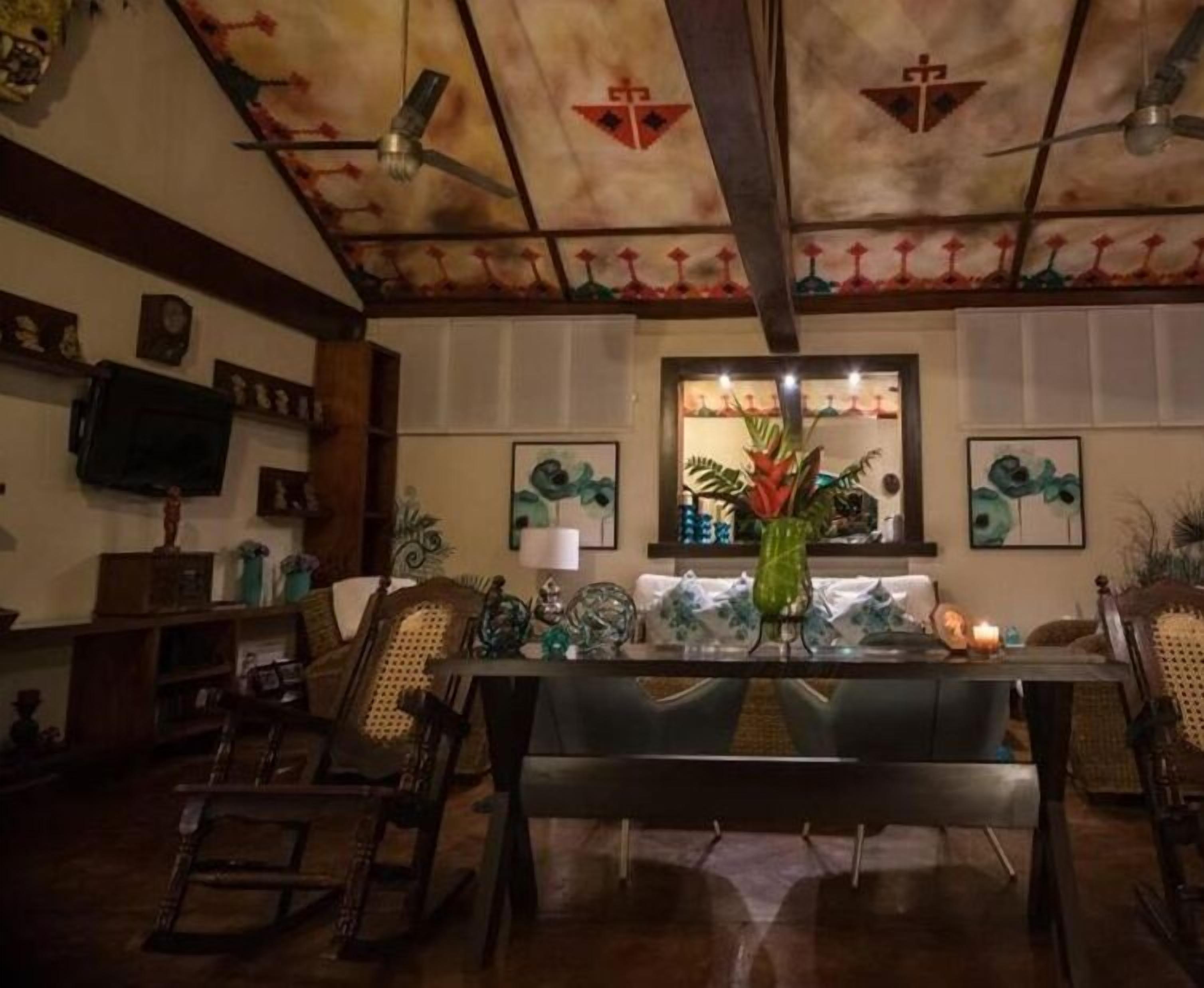 Un espace repas comprenant une longue table, des chaises, un vase avec des fleurs et des ventilateurs de plafond.