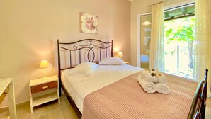 A bedroom with a bed, bedside lamps, a nightstand, a window with curtains, and a wall-mounted picture. - Asteraki Beach House (Acharavi)