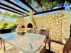 An outdoor patio with a stone wall, a glass table, wicker chairs, and a pizza oven.
