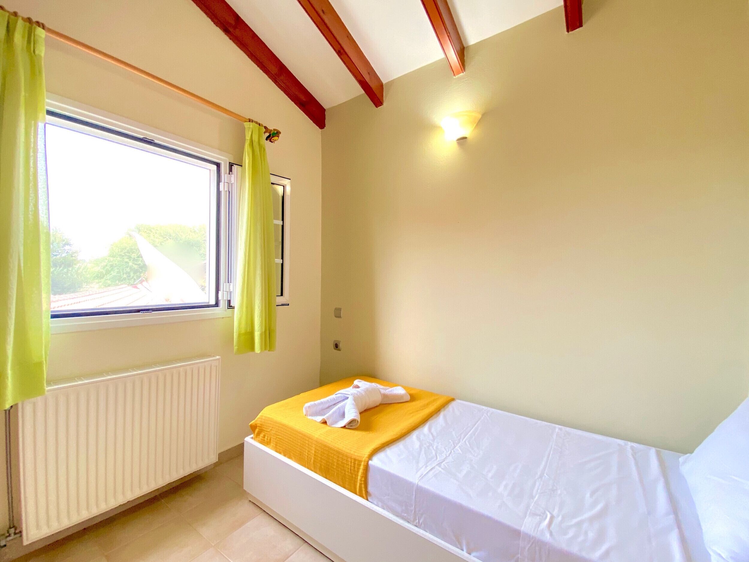 A small, single-bed room with a window, a radiator, and a ceiling light.