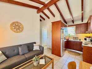 A modern living room with a sofa, a coffee table, and a kitchen area with wooden cabinets and a refrigerator. - Asteraki Poolside Apartment (St. Stefanos Bay)