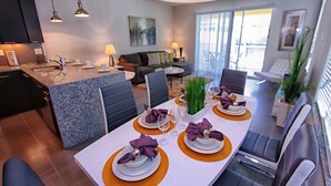 Une cuisine moderne dotée d’un îlot central, d’un coin repas avec une table pour quatre personnes et d’un salon avec un canapé et une table basse.