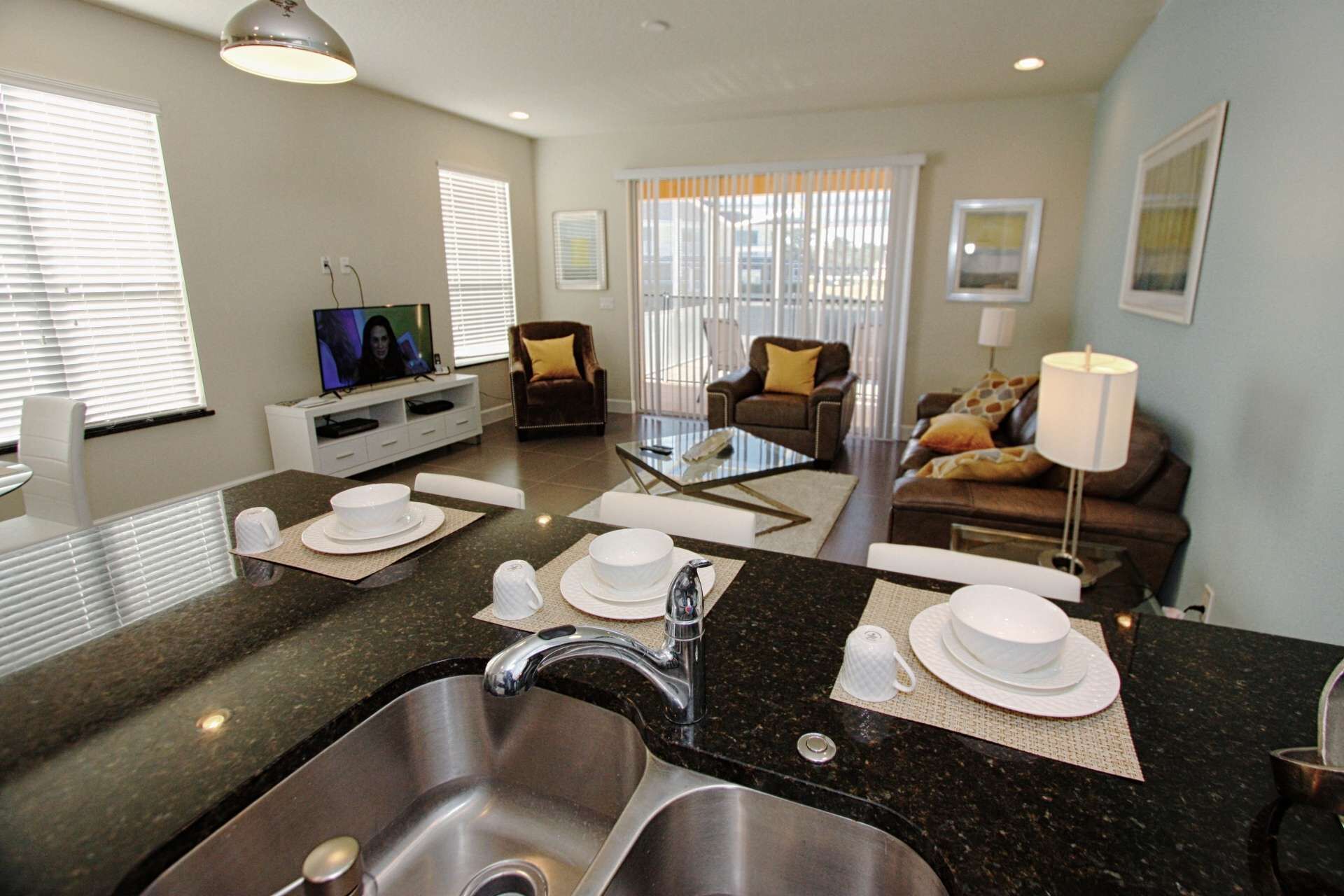 A modern kitchen with a granite countertop, stainless steel sink, and a dining area with a glass coffee table.