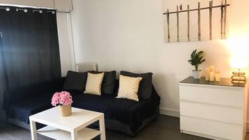 Un salon moderne avec un canapé noir, une table d’appoint blanche et une commode blanche.