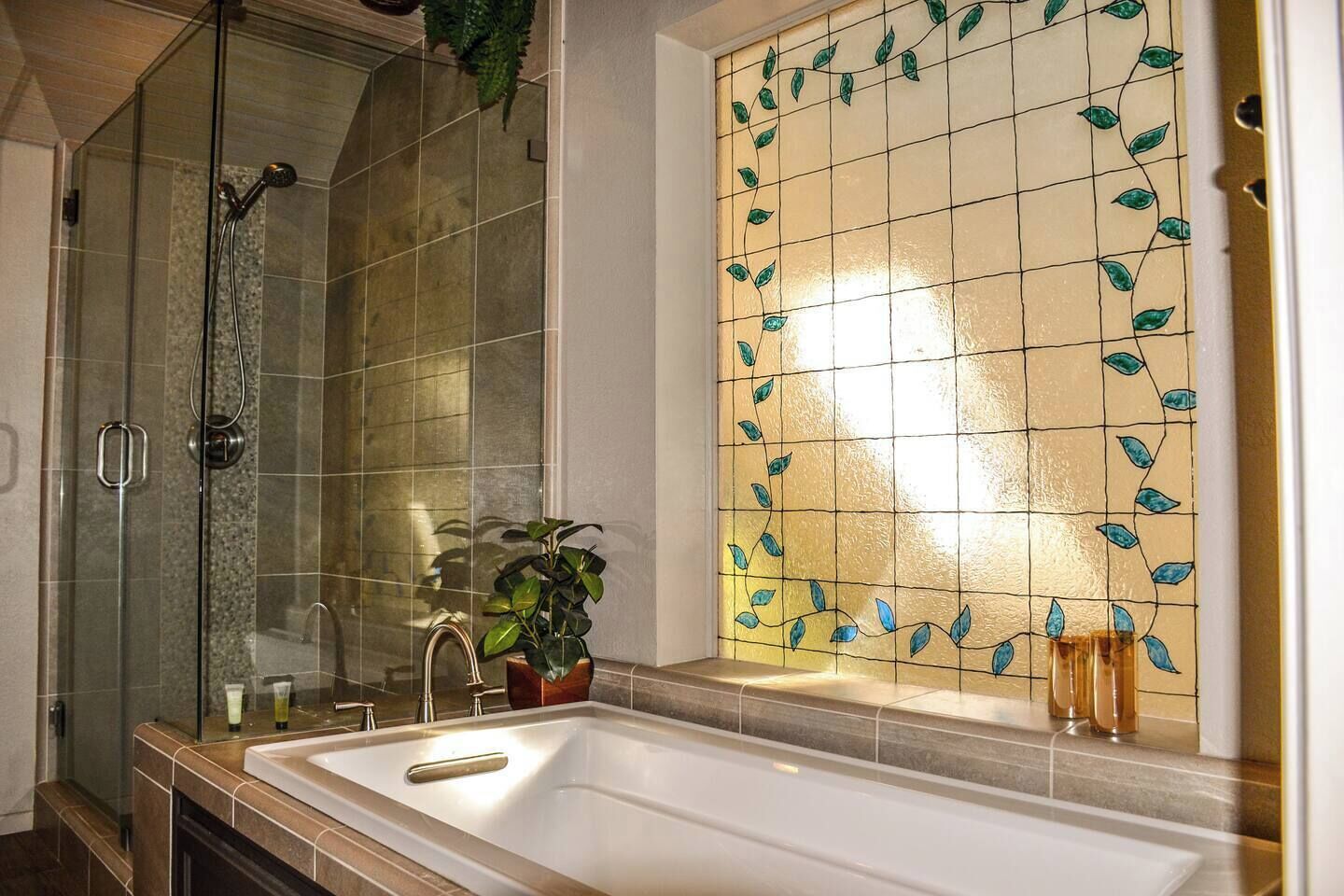 A bathroom with a glass shower enclosure, a bathtub, and a tiled wall with a leaf pattern.