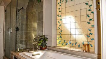 A bathroom with a glass shower enclosure, a bathtub, and a tiled wall with a leaf pattern.