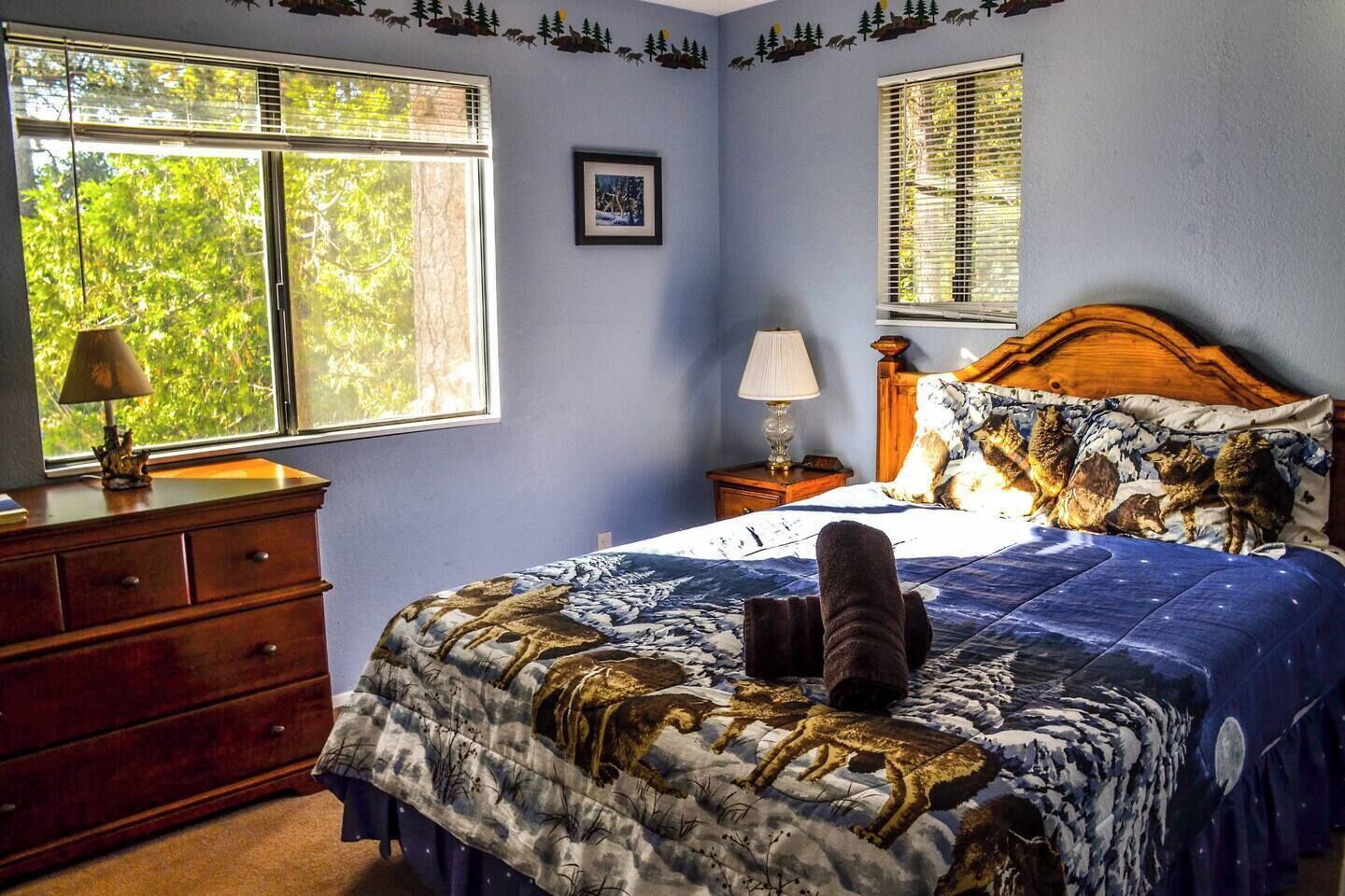A bedroom with a bed, dresser, nightstand, and two windows.