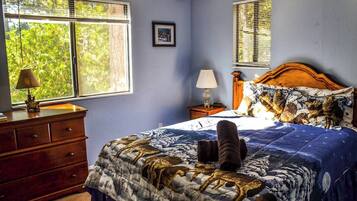 A bedroom with a bed, dresser, nightstand, and two windows.