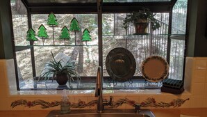 Een keuken met een roestvrijstalen spoelbak, een raam met decoratieve kerstbomen en uitzicht op een bos.