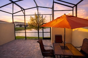 A patio with a table and chairs, an umbrella, and a view of a lake and buildings. - 3207 Compass Bay (Kissimmee)