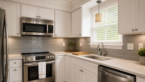 A modern kitchen with stainless steel appliances, white cabinetry, a window with blinds, and a small plant on the counter. - Walk to restaurants! 10min to beaches and downtown Charleston.  (Mount Pleasant)