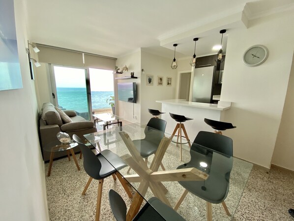 A modern dining area with a glass table and black chairs, a sofa, and a view of the ocean. - Nice apartment on the beach with a large terrace facing the sea (La Garita)