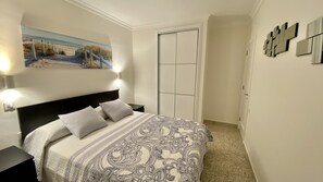 A bedroom with a bed, two bedside tables, a nightstand, a painting on the wall, and a door. - Nice apartment on the beach with a large terrace facing the sea (La Garita)