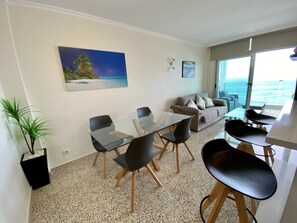 A modern living room with a glass dining table, black chairs, a beige sofa, and a large window overlooking the sea. - Nice apartment on the beach with a large terrace facing the sea (La Garita)