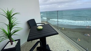 Ein Balkon mit Tisch und Stuhl, einer Topfpflanze und Blick auf Strand und Meer.