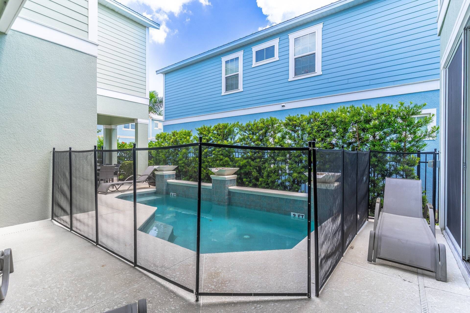 Une piscine dotée d’une enceinte en verre, entourée d’une clôture métallique, et située à côté d’un bâtiment dont le revêtement extérieur est bleu.