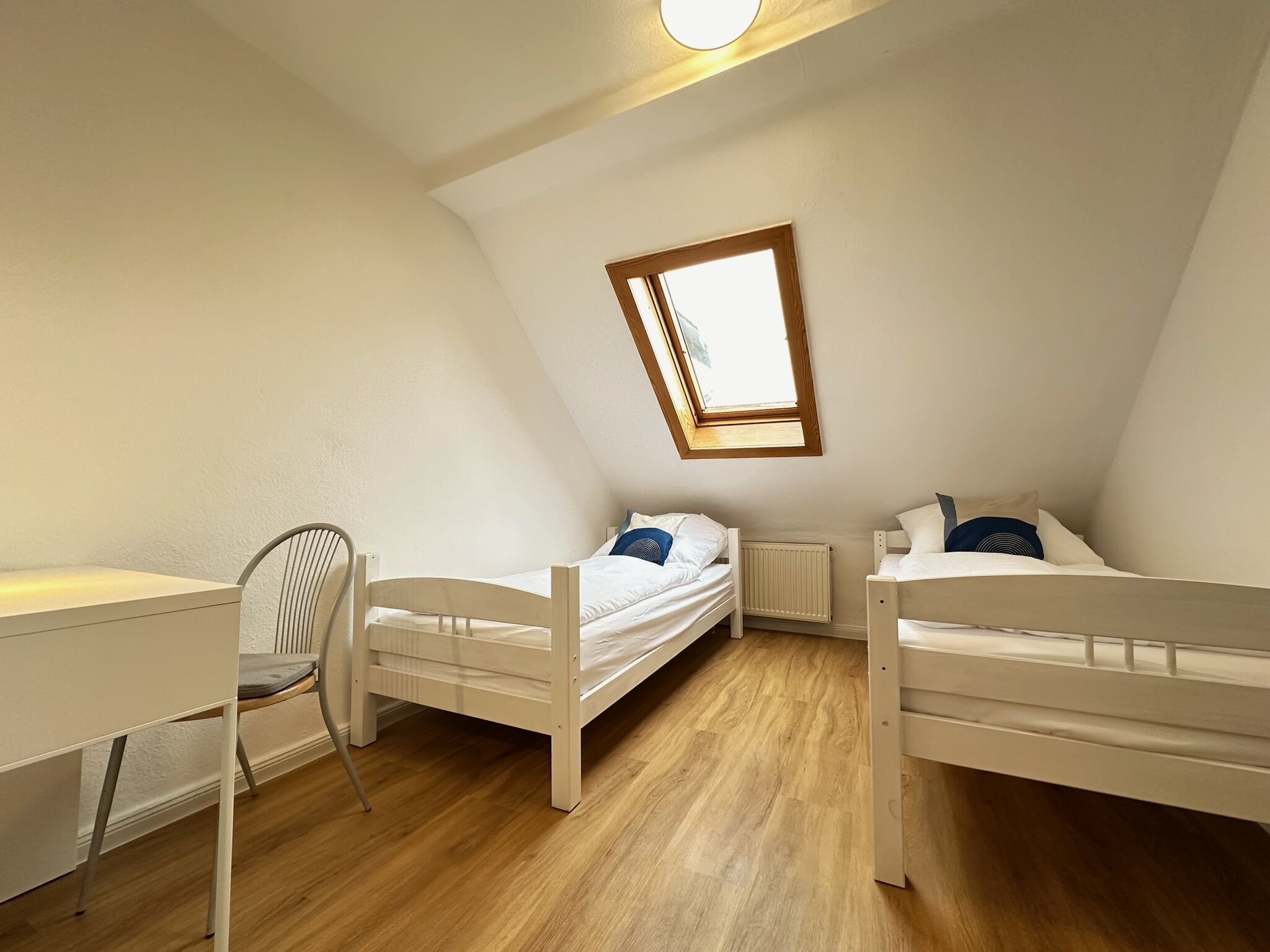A dormitory room with two bunk beds, a desk, and a chair.