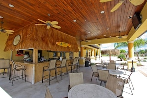 Relax in a shaded outdoor seating area with tables and chairs, surrounded by palm trees and a clear view of the landscape.