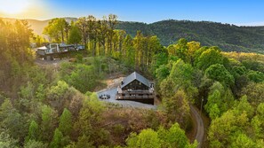 A lodge with a large deck, surrounded by dense forest and hills. - YARD/Hot Tub/Game Room/Theater/VIEWS/Fire Pit - Garrett Lodge (Gatlinburg)