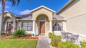 Una casa de dos pisos con fachada color beige, una puerta frontal marrón y un pequeño patio con mobiliario exterior.