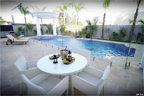 Relax by the pool surrounded by lush greenery and a pergola.