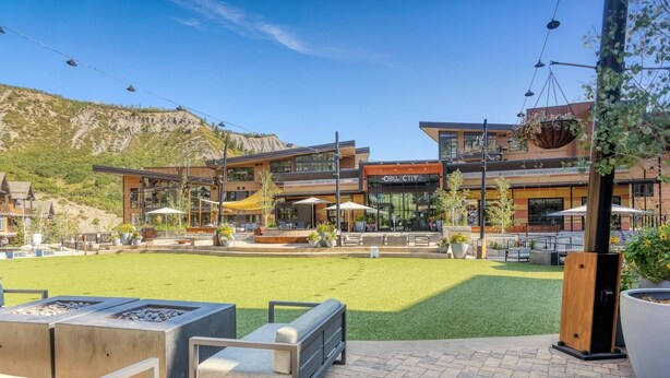A modern outdoor seating area with fire pits, a grassy lawn, and a building with a 'COLLECTIVE' sign. - Base Village (Snowmass Village)