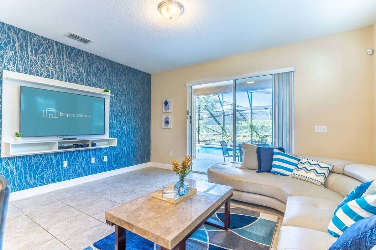 A living room with a TV, a sofa, a coffee table, and a view of a swimming pool.
