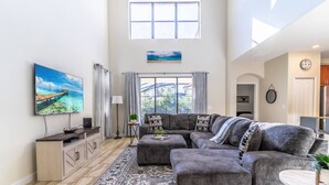 A spacious living room with a large sectional sofa, a flat-screen TV, a wooden cabinet, and a patterned rug. - 4627 Solterra (Davenport)