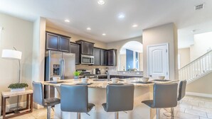 A modern kitchen with dark cabinets, stainless steel appliances, and a central island with bar stools. - 4627 Solterra (Davenport)