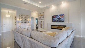Un salon moderne avec un grand canapé d’angle, une cheminée et un téléviseur fixé au mur.