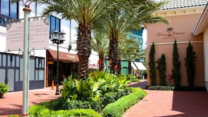 Un espace extérieur bien entretenu, agrémenté de palmiers, d’un chemin en briques et d’un bâtiment portant l’inscription « Tommy Bahama Tropical Café ».