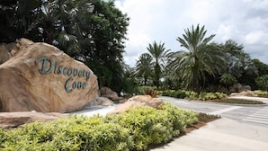 A large rock with "Discovery Cove" written on it, surrounded by lush greenery and palm trees. - 2633 Trafalgar Village (Kissimmee)