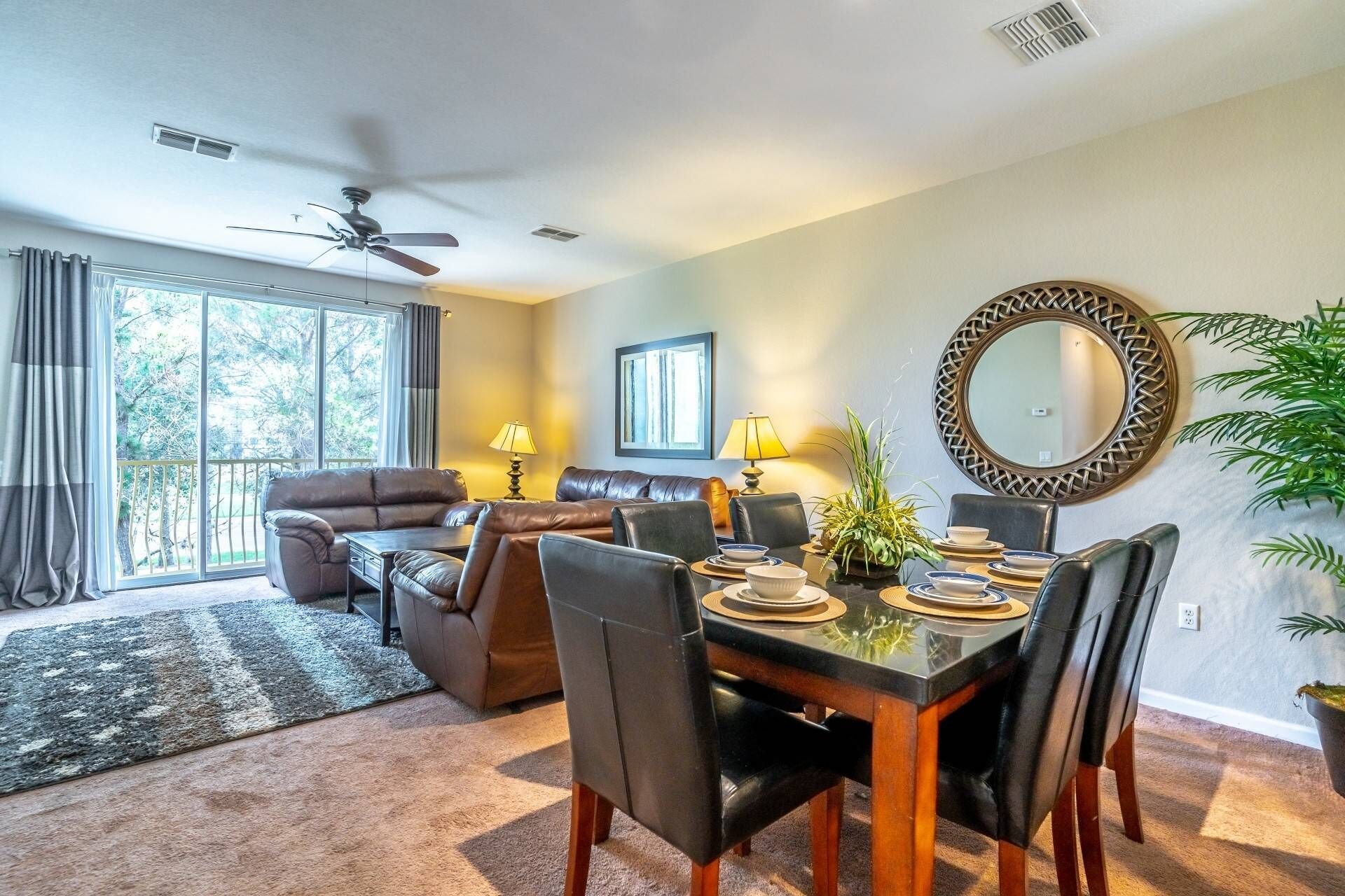 A spacious living room with a dining area, large windows, and a ceiling fan.