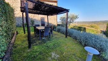 Un edificio de piedra con una pérgola de madera y una mesa con sillas en el jardín.