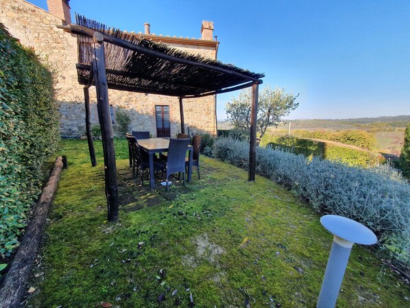 Ein Steinhaus mit einer Holzpergola und einem Tisch mit Stühlen im Garten.