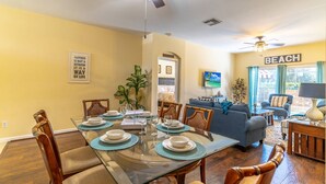 A dining area with a glass table set for six, surrounded by wooden chairs. A blue sofa and a small table with a lamp are in the background. - 8118 Windsor Palms (Kissimmee)