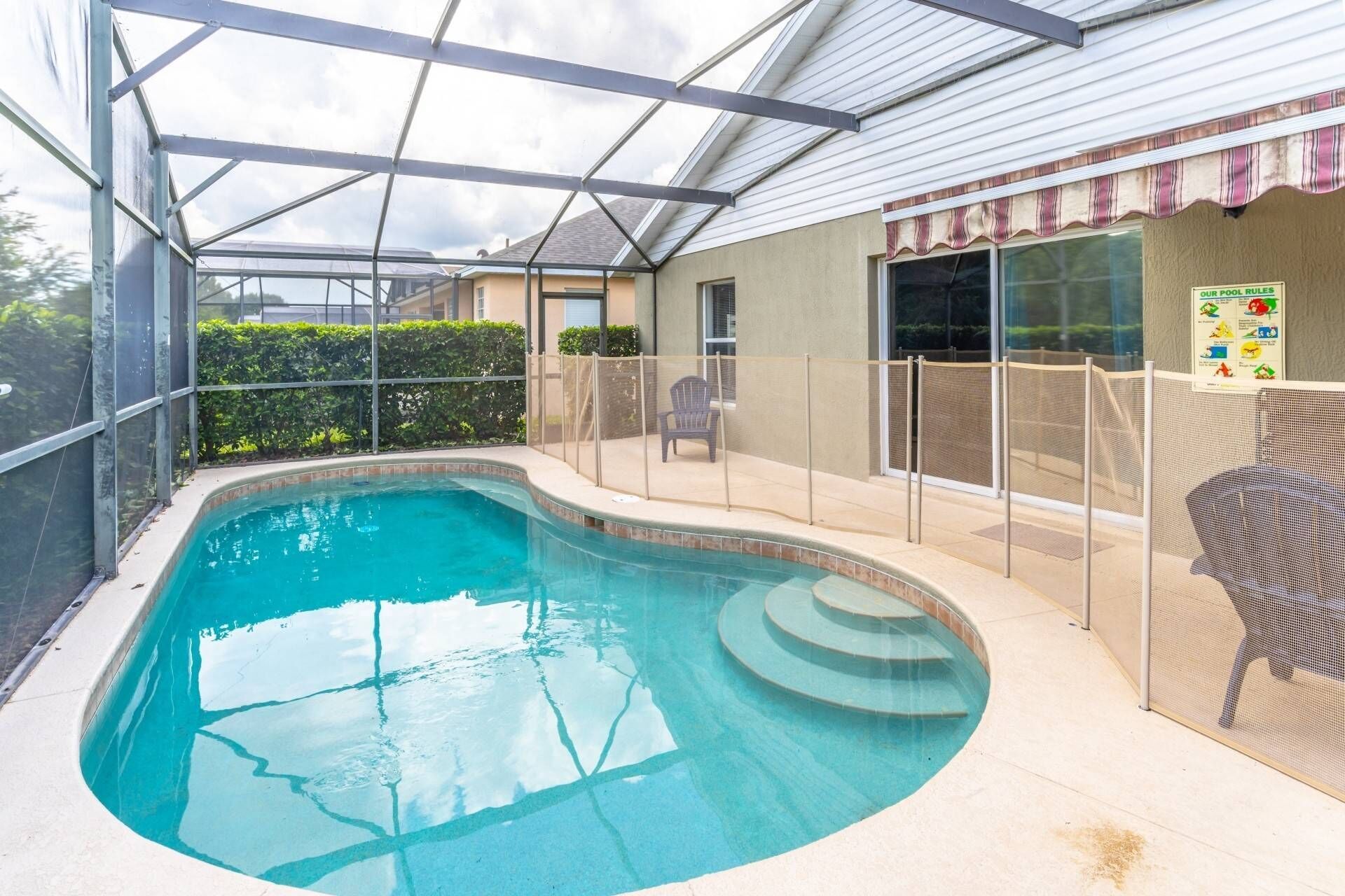 A swimming pool with a glass enclosure, a covered patio, and a chair.