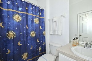 A bathroom with a blue shower curtain featuring sun and moon patterns, a white toilet, a sink with soap dispensers, and a mirror above the sink. - 7669 Windsor Hills (Kissimmee)