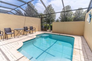 A swimming pool with a glass enclosure, surrounded by a beige wall and a brick patio. - 7669 Windsor Hills (Kissimmee)