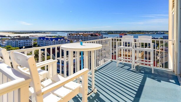 A balcony with white chairs and a small table, overlooking a coastal area with buildings and a body of water. - 🏖️Fabulous Ocean Views in Belmont Towers on Boardwalk. AC, Pool, Gym🏖️ (Ocean City)