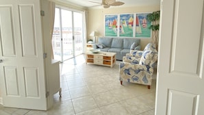 A spacious living room with a large window, a ceiling fan, and a painting of sailboats. - 🏖️Fabulous Ocean Views in Belmont Towers on Boardwalk. AC, Pool, Gym🏖️ (Ocean City)