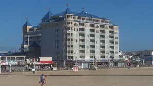 A large hotel with multiple floors and balconies, located near a beach with a sandy shore. - 🏖️Fabulous Ocean Views in Belmont Towers on Boardwalk. AC, Pool, Gym🏖️ (Ocean City)