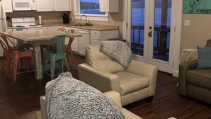 A living room with a sofa, a chair, and a dining area with a table and chairs. There is a kitchen with white cabinets and a microwave.