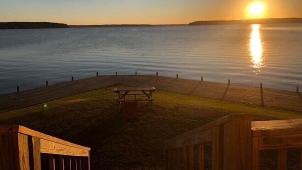 A wooden deck overlooking a calm body of water during sunset.